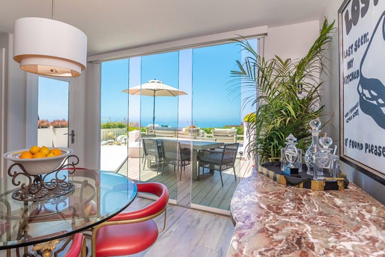 Dining room with staggered frameless glass doors with unobstructed views of table on patio and ocean.