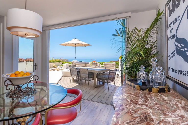 Dining room with stacked frameless glass doors on the right of the doorframe with unobstructed views of the table on patio and the ocean.