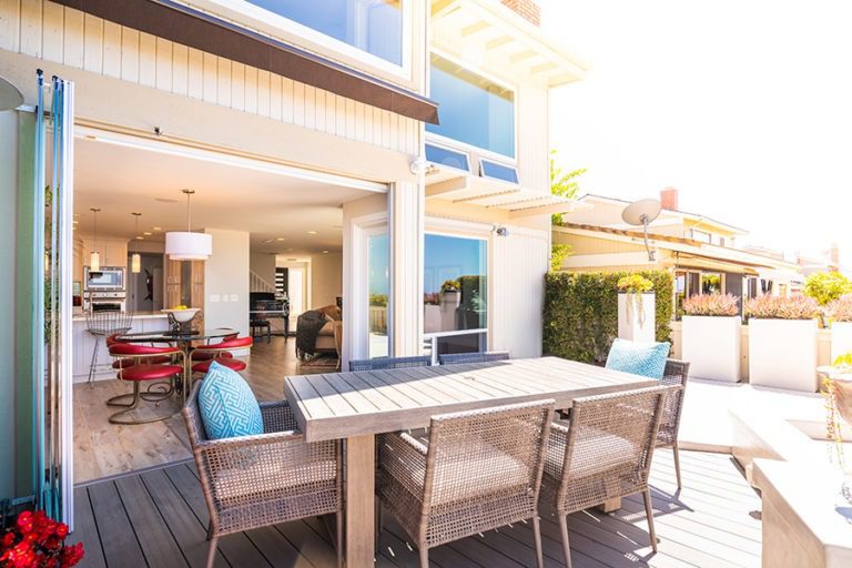 Outdoor space with patio table and stacked frameless glass doors looking into the dining room.