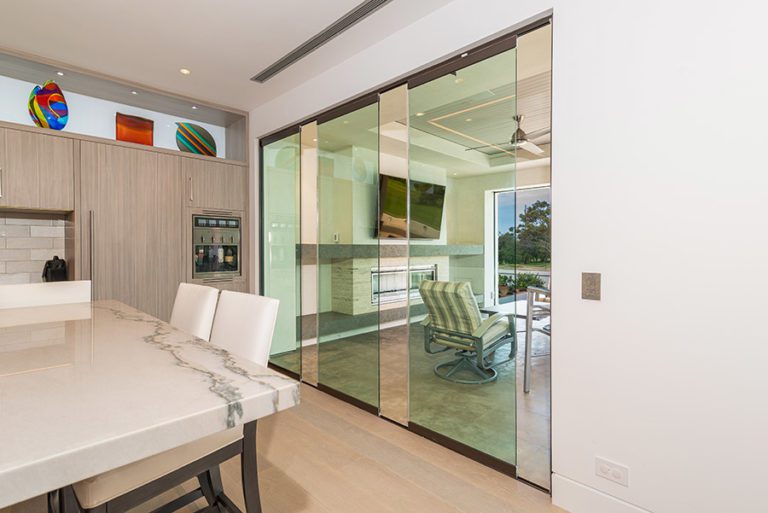 Partially open frameless sliding glass doors separating kitchen area from outdoor patio.