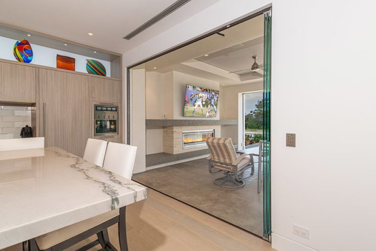 Fully open frameless sliding glass doors connecting kitchen area with patio.