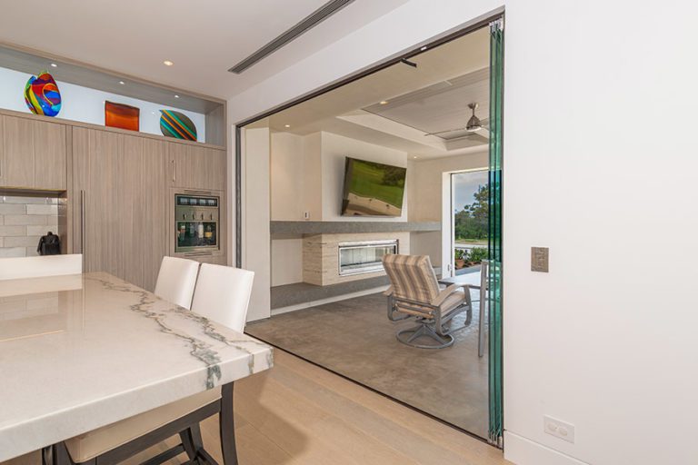 Stacked frameless glass doors on the right of the doorframe connecting kitchen area with patio.