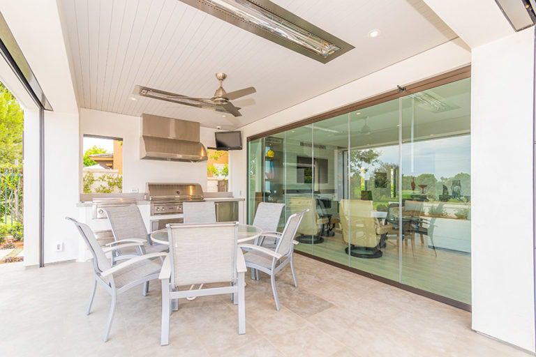 Outdoor space with round patio table and kitchenette next to closed frameless glass doors.