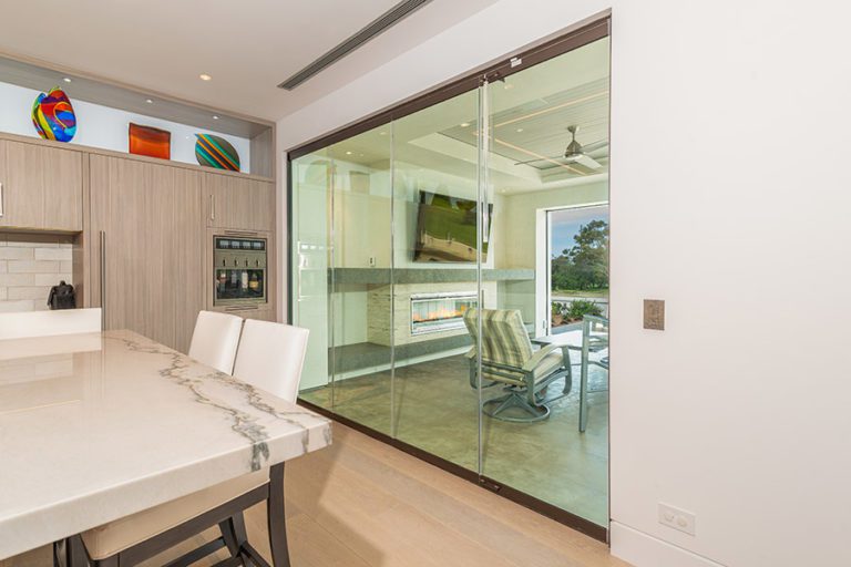 Closed frameless sliding glass doors separating kitchen area with marble table from outdoor patio.