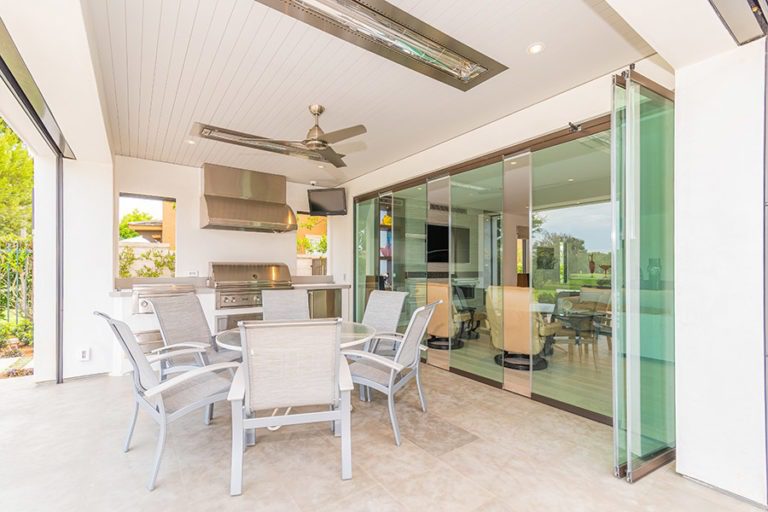 Outdoor space with round patio table and kitchenette next to partially closed frameless glass doors.