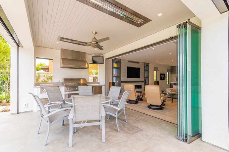 Outdoor space with round patio table and stacked frameless glass doors looking into the living room.