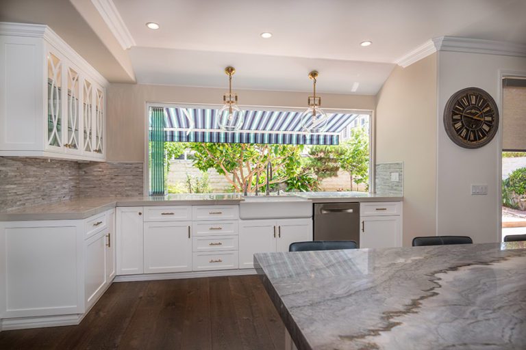 Frameless glass sliding windows stacked to one side of window frame on top of marble kitchen countertops next to kitchen island.