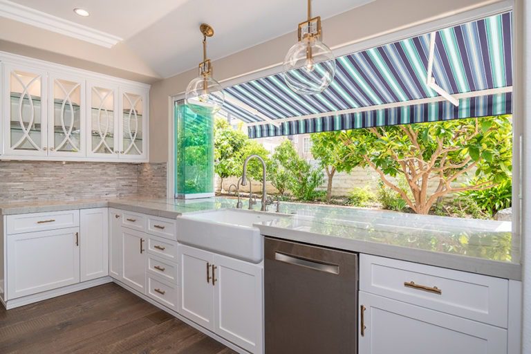 Marbled kitchen counter top with frameless glass door stacked to one side of window frame with unobstructed views of plants in backyard.