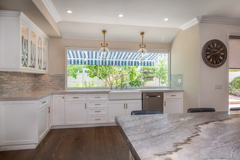 Frameless glass sliding windows with marbled kitchen countertops and kitchen island with wood floor.