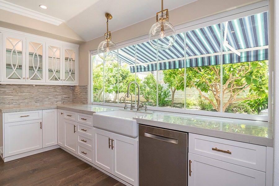 Enclosed frameless glass windows on top of marbled kitchen countertop with an unobstructed view of plants in backyard.