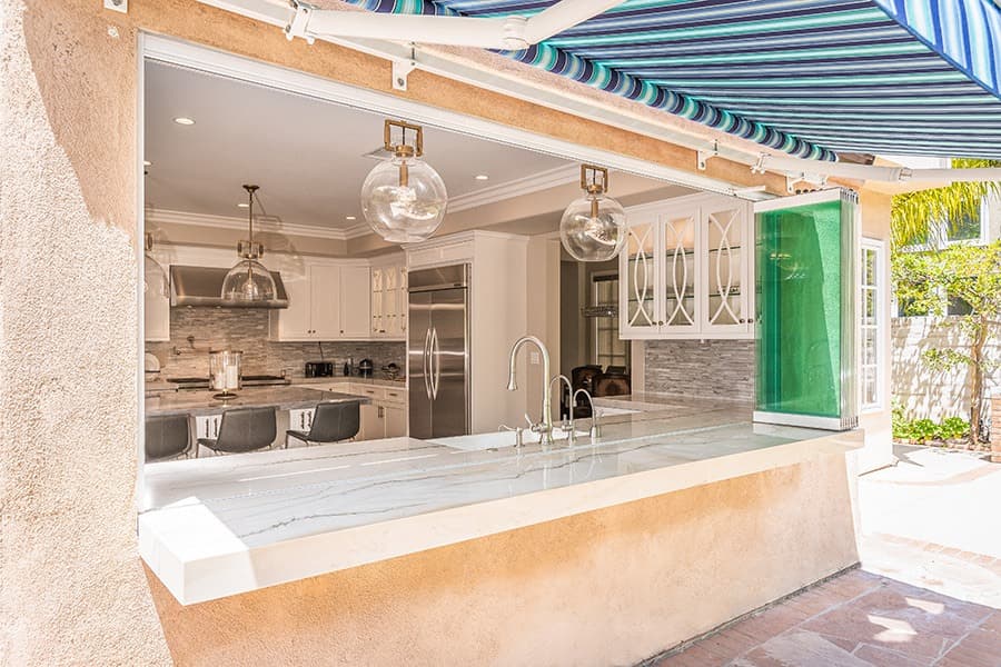 Looking into kitchen from backyard with stacked frameless glass windows on top of marble kitchen countertop.