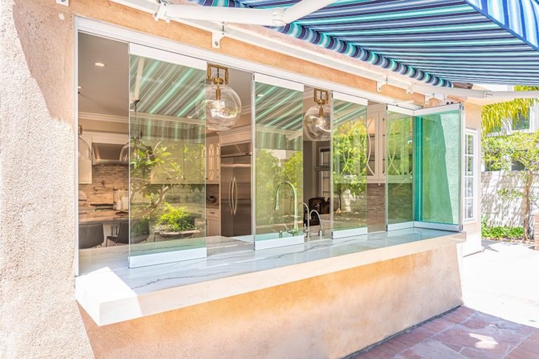 Looking into kitchen from backyard with staggered frameless glass windows on top of marble kitchen countertop.