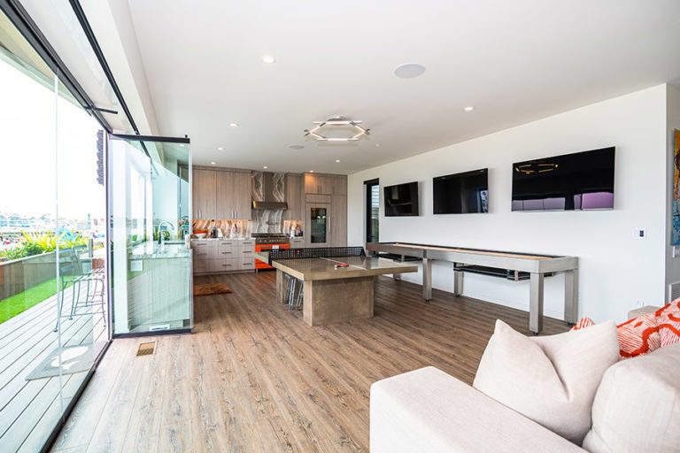 House open concept living room and kitchen with ping pong table centered in room and enclosed frameless glass doors on the left.