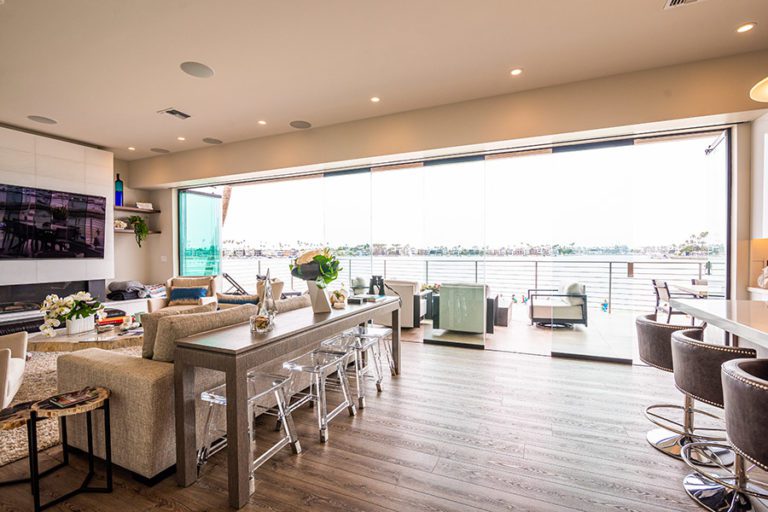 Open concept living room and kitchen with wood flooring and staggered frameless glass sliding doors with unobstructed views of the water.