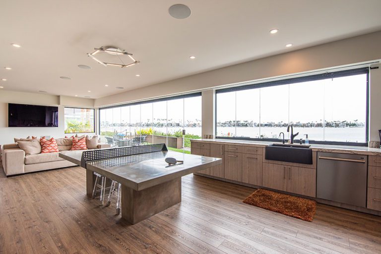 Ping pong table center of open concept kitchen and living room with enclosed frameless glass doors and windows.