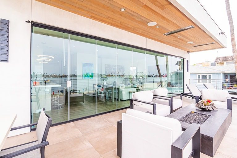 Marble floored patio with fire place looking into open concept of living room and kitchen with frameless glass doors enclosed with an unobstructed view of the inside.