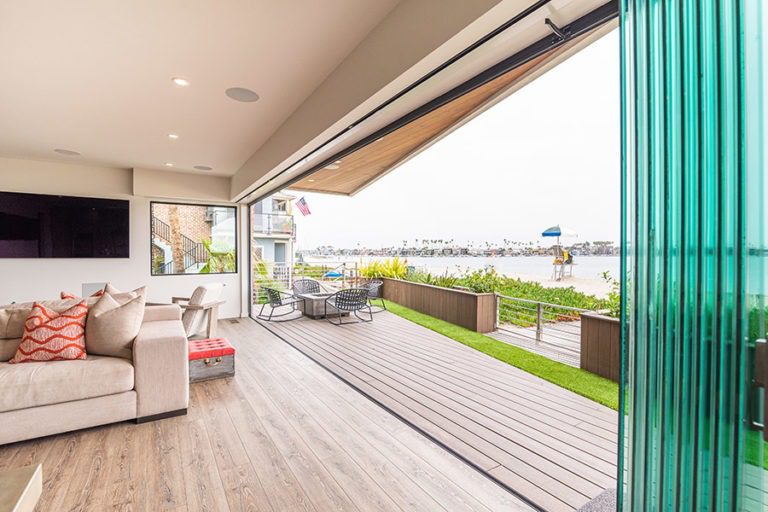 Stacked frameless glass doors to right side of frame allowing for views of the living room and wooden floor patio with fire pit.