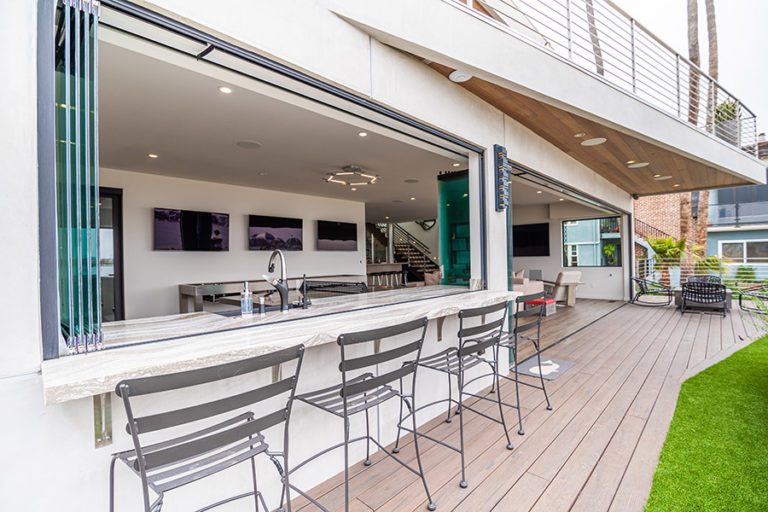 Patio view looking into open concept kitchen and living room with frameless glass doors and windows stacked to one side.