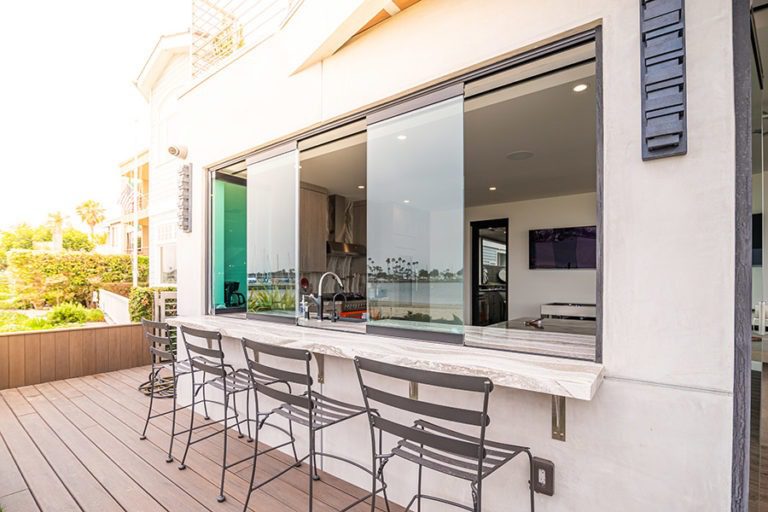 The frameless glass window is staggered ontop of the kitchen counter while looking into the open concept kitchen from the wooded patio floor.