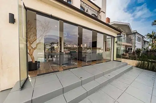 Partially open frameless sliding glass doors connecting living room with patio.